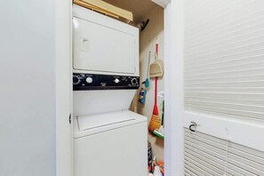 A laundry room with a washing machine and dryer, a broom, and cleaning supplies. - Ocean Retreat Unit N1 (North Myrtle Beach)