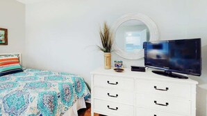 A bedroom with a bed, a television on a dresser, a mirror, and a plant. - Ocean Retreat Unit N1 (North Myrtle Beach)