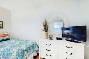 A bedroom with a bed, a television on a dresser, a mirror, and a plant. - Ocean Retreat Unit N1 (North Myrtle Beach)
