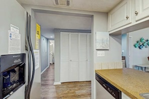 Eine Küche mit eingebautem Geschirrspüler, Kühlschrank und Mikrowelle. Ein Holzboden und eine weiße Tür sind im Hintergrund zu sehen.