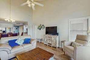 Ein Wohnzimmer mit Sofa, Sessel, Couchtisch, Fernseher und Deckenventilator.
