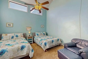 Ein Schlafzimmer mit zwei Betten, einem Deckenventilator, einem Fenster und einem Ledersofa.