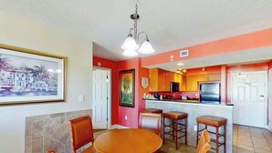 A dining area with a round table and chairs, a kitchen with red walls, and a bar area. - Bahama Sands Unit 0701 (North Myrtle Beach)