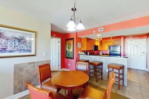 A dining area with a round table and chairs, a kitchen with red walls, and a bar area. - Bahama Sands Unit 0701 (North Myrtle Beach)
