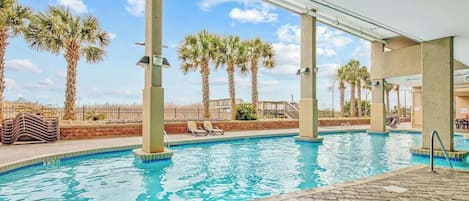 An indoor swimming pool with clear blue water, surrounded by palm trees and lounge chairs.