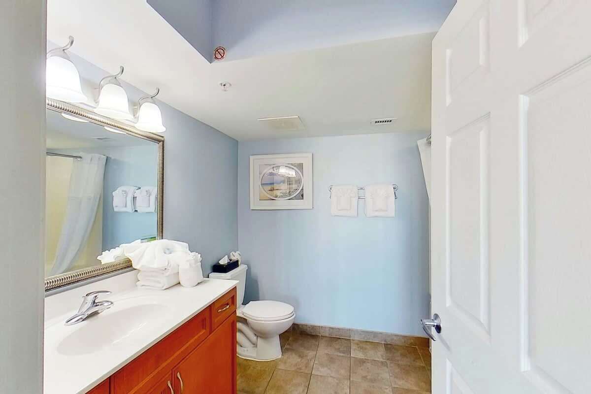 A bathroom with a white sink, a mirror with lights, a toilet, and a towel rack.