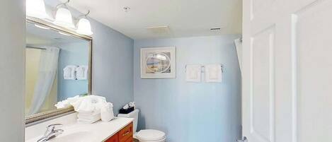 A bathroom with a white sink, a mirror with lights, a toilet, and a towel rack.