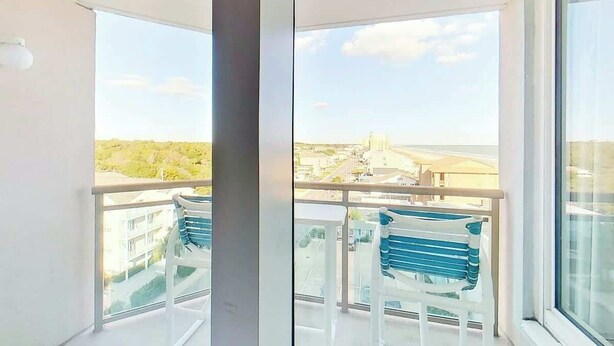 A balcony with a view of a cityscape, a white chair, and a blue chair. - Bahama Sands Unit 0701 (North Myrtle Beach)