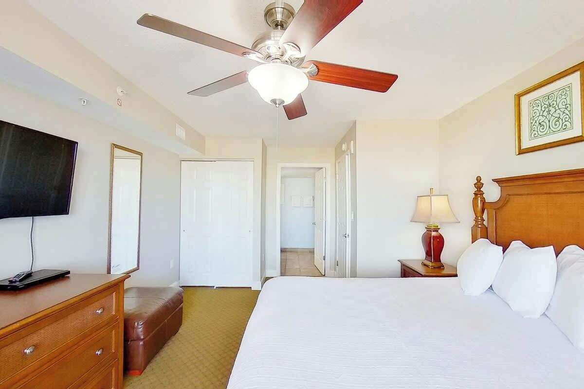 Habitación de hotel con cama, televisor, escritorio, lámpara y ventilador de techo.