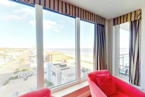 A hotel room with large windows, a red sofa, and a view of the cityscape. - Bahama Sands Unit 0701 (North Myrtle Beach)