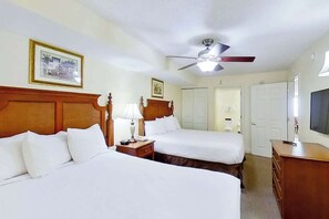 Ein Hotelzimmer mit zwei Betten, einem Deckenventilator, einem Fernseher und einer hölzernen Kommode.