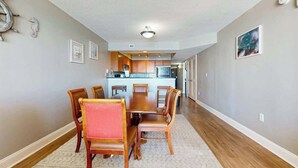 A dining area with a wooden table and chairs, a kitchen in the background, and a hallway leading to other rooms. - Bahama Sands Unit 0707 (North Myrtle Beach)