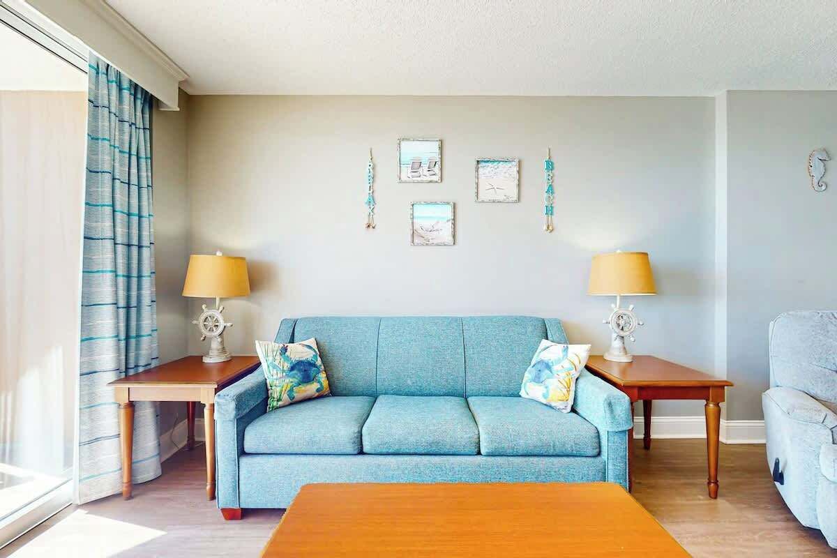 A living room with a blue sofa, two side tables with lamps, and wall art.