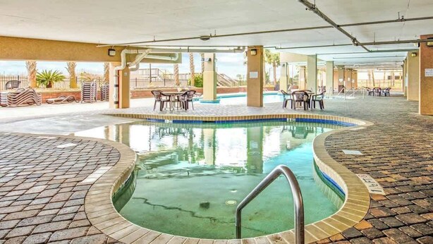 En indendørs swimmingpool med flisebelagt solterrasse, omgivet af liggestole og borde.