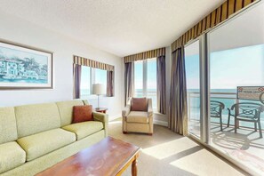 Ein Hotelzimmer mit Sofa, Ohrensessel und Meerblick durch große Fenster.