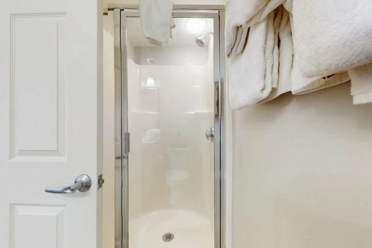 A glass-enclosed shower stall with a white door and a towel rack above it.