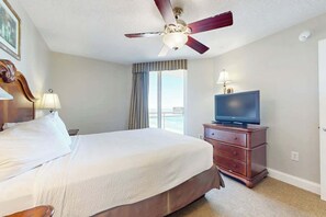 Ein Hotelzimmer mit Bett, Fernseher auf einem Schminktisch, Deckenventilator und einem Fenster mit Vorhängen.