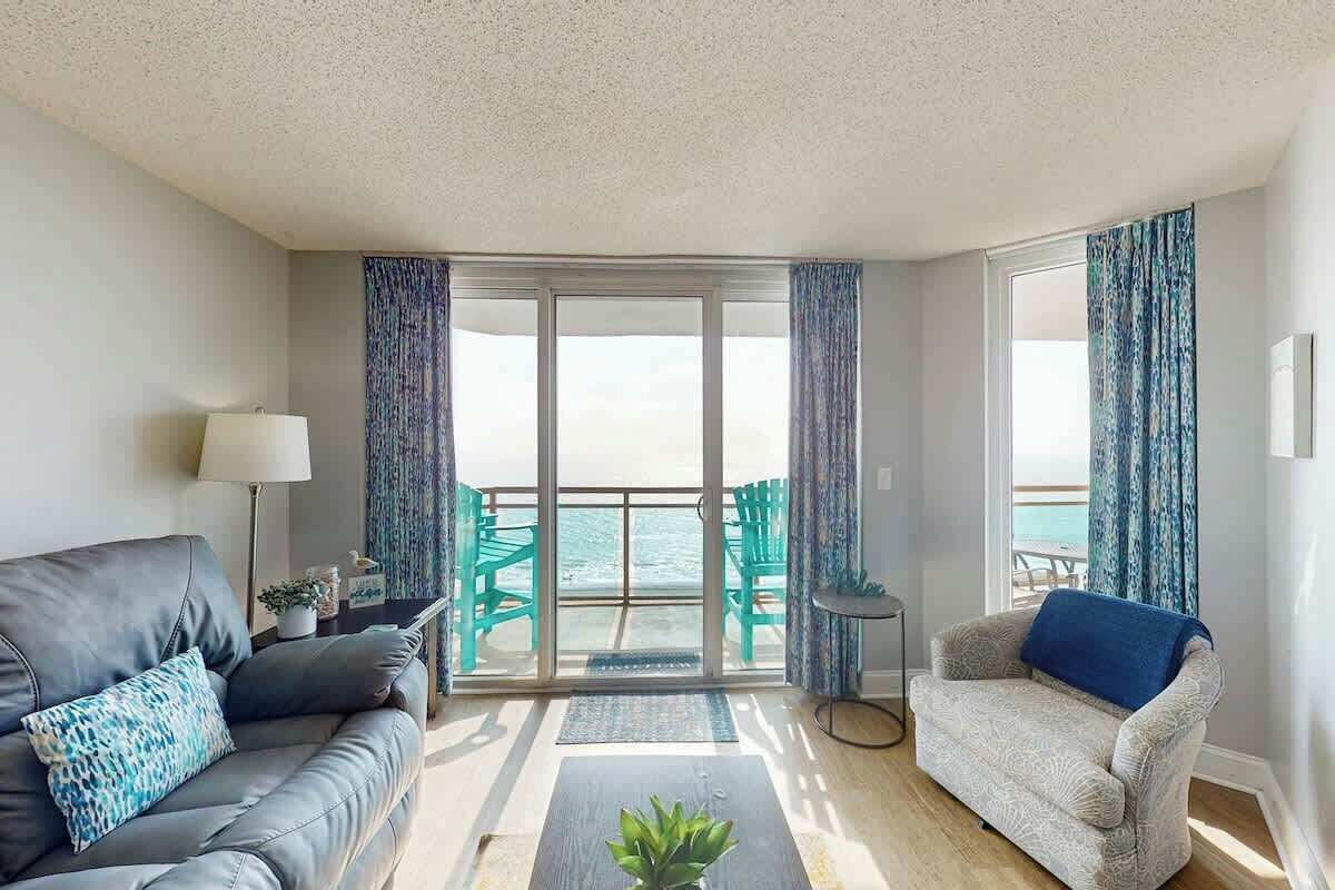 Un salón con sofá, sillón y vista al mar a través de un ventanal.