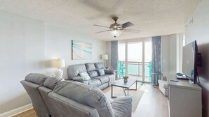 Un salon moderne avec un canapé d’angle, un téléviseur à écran plat et un ventilateur de plafond.