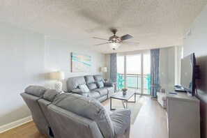 A modern living room with a sectional sofa, a flat-screen TV, and a ceiling fan. - Bahama Sands Unit 0806 (North Myrtle Beach)