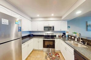 A modern kitchen with white cabinets, stainless steel appliances, a microwave, oven, and a sink. - Bahama Sands Unit 0806 (North Myrtle Beach)