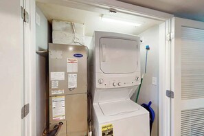 Une buanderie équipée d’un lave-linge et d’un sèche-linge superposés, d’un meuble de rangement et d’une serpillière bleue.