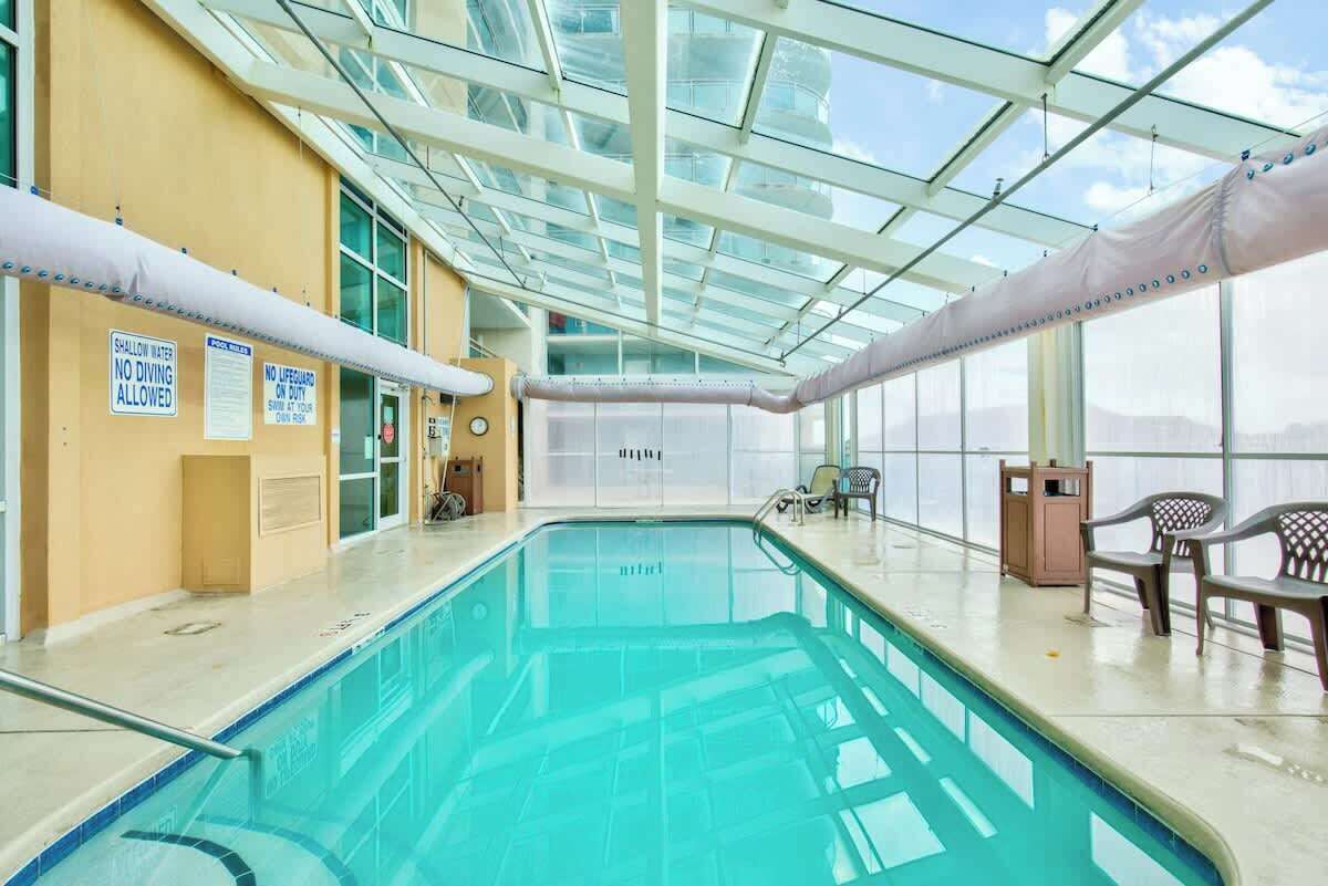 Ein hallenbad mit klaren Glasdecken, Schildern, die für flaches Wasser und Tauchenverbot weisen, und Blick auf den Himmel.