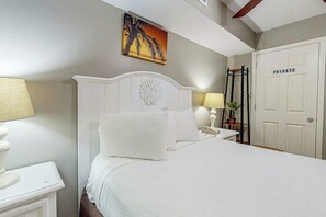 A hotel room with a bed, bedside tables, a lamp, a painting, and a private door. - Bahama Sands Unit 0807 (North Myrtle Beach)
