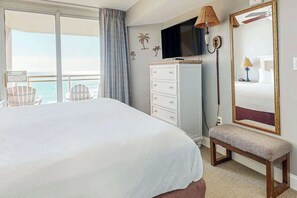 A hotel room with a large bed, a television, a bench, a dresser, and a view of the ocean. - Bahama Sands Unit 0807 (North Myrtle Beach)
