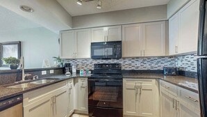 A modern kitchen with white cabinets, a black microwave, and a stainless steel refrigerator. - Bahama Sands Unit 0807 (North Myrtle Beach)