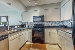 A modern kitchen with white cabinets, a black microwave, and a stainless steel refrigerator. - Bahama Sands Unit 0807 (North Myrtle Beach)