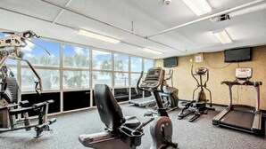 A gym with various exercise equipment, large windows, and a television on the wall. - Bahama Sands Unit 0807 (North Myrtle Beach)
