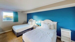 Een hotelkamer met twee bedden, een raam met gordijnen, een nachtkastje en een witte plank.