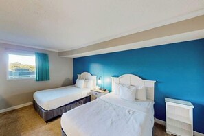 Ein Hotelzimmer mit zwei Betten, einem Fenster mit Vorhängen, einem Nachttisch und einem weißen Regal.