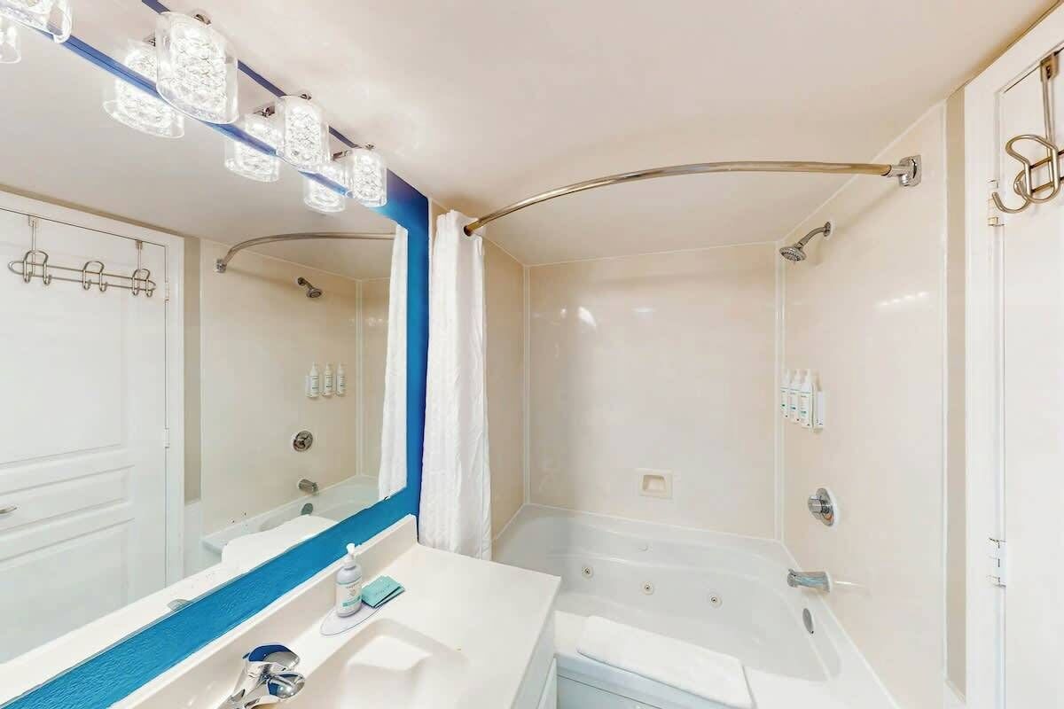 Une salle de bain avec un lavabo blanc, un miroir, une douche et une baignoire.