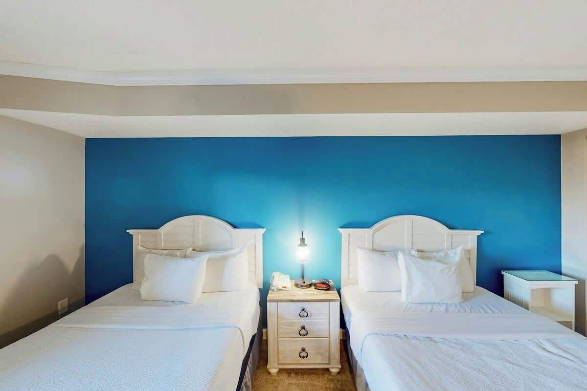 Una habitación de hotel con dos camas individuales, una mesita de noche con lámpara y un atril con teléfono.
