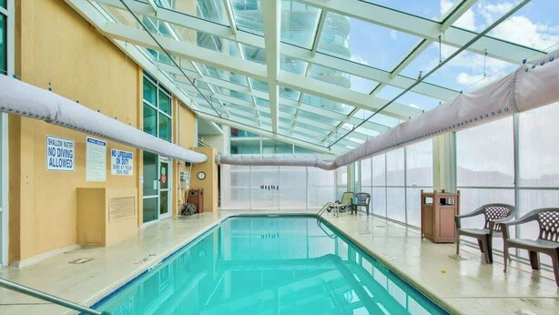 Ein Hallenbad mit klaren Glasdecken, Sicherheitshinweisen und Sitzbereichen.