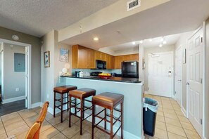 A kitchen with wooden cabinets, a black refrigerator, and a bar area with stools.