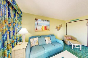 A room with a blue sofa, a small table, a lamp, a painting, and a sign on the wall. - Bay Watch Resort 0407 (North Myrtle Beach)