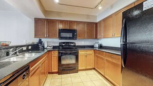 A kitchen with wooden cabinets, a black refrigerator, a microwave, and a stove. - Bahama Sands Unit 0905 (North Myrtle Beach)