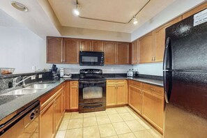 A kitchen with wooden cabinets, a black refrigerator, a microwave, and a stove. - Bahama Sands Unit 0905 (North Myrtle Beach)