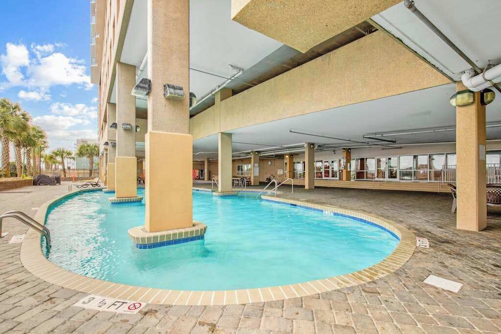 An indoor swimming pool with a tiled edge, surrounded by a brick floor and supported by concrete pillars.