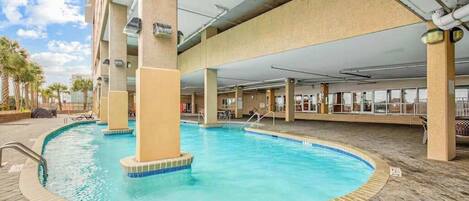 An indoor swimming pool with a tiled edge, surrounded by a brick floor and supported by concrete pillars.