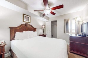 A hotel room with a large bed, a ceiling fan, a dresser, a television, and a door leading to a bathroom. - Bahama Sands Unit 0905 (North Myrtle Beach)