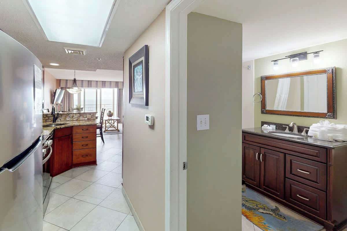 A hotel room with a kitchen area, a bathroom with a large mirror, and a dining area with a view.