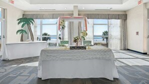 Um quarto com uma mesa posta para um casamento, grandes janelas e vista para a praia.