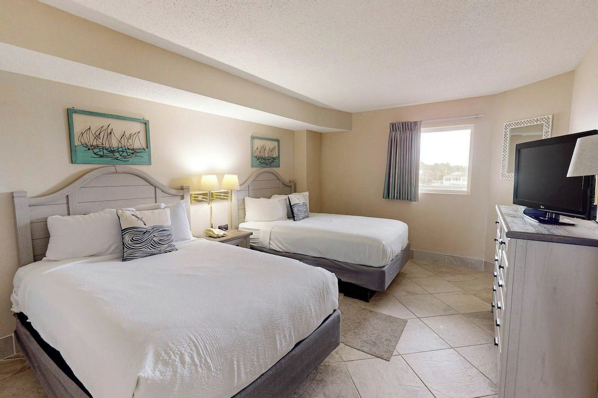 A hotel room with two beds, a television, and artwork on the walls.