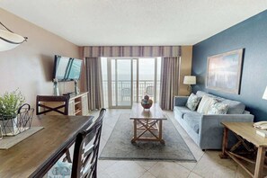 Ein Wohnzimmer mit Essbereich, einer Couch, einem Fernseher und einem Balkon mit Blick.