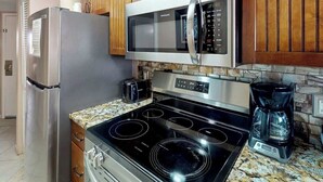 Uma cozinha equipada com geladeira de aço inoxidável, micro-ondas, fogão por indução e cafeteira.