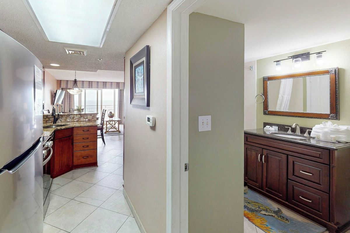 A modern kitchen with a built-in refrigerator, a dining area with a chandelier, and a bathroom with a large mirror and dark wooden cabinets.